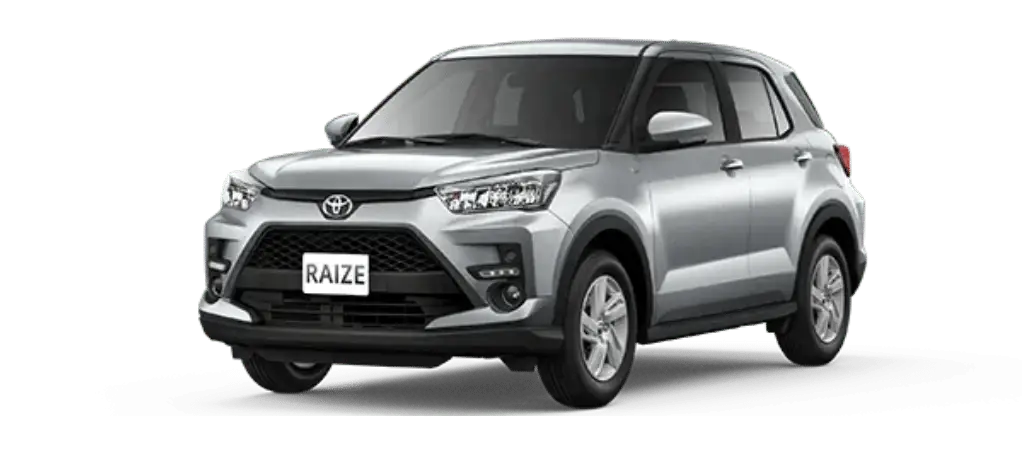 Toyota Raize exterior 1 – Driveinbali.com The Toyota Raize, a silver compact SUV with a modern design, features sleek headlights and a black grille. This stylish vehicle is parked against a plain background, proudly displaying its RAIZE license plate.